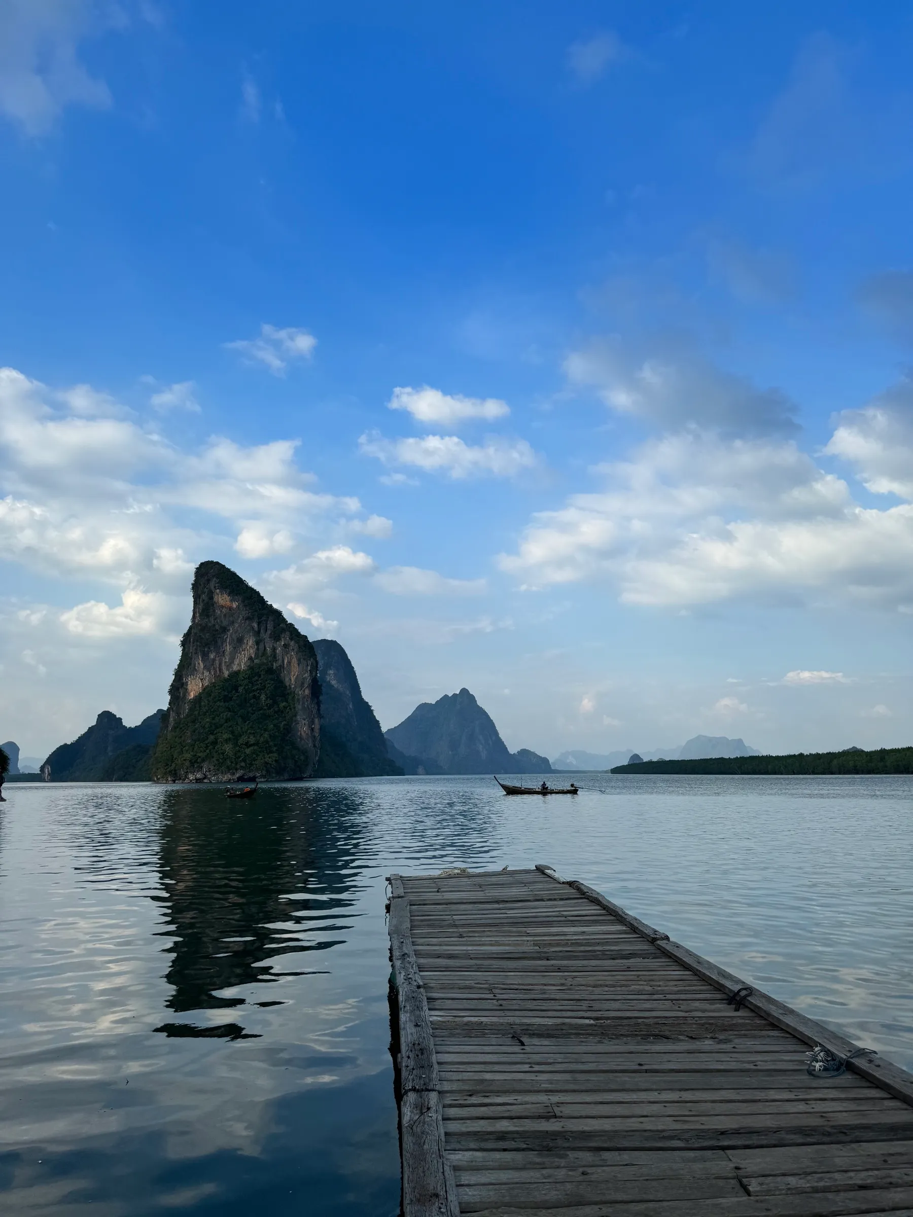 Un ponton de bois avance vers les pitons karstiques d'une baie calme, sous un grand ciel bleu
