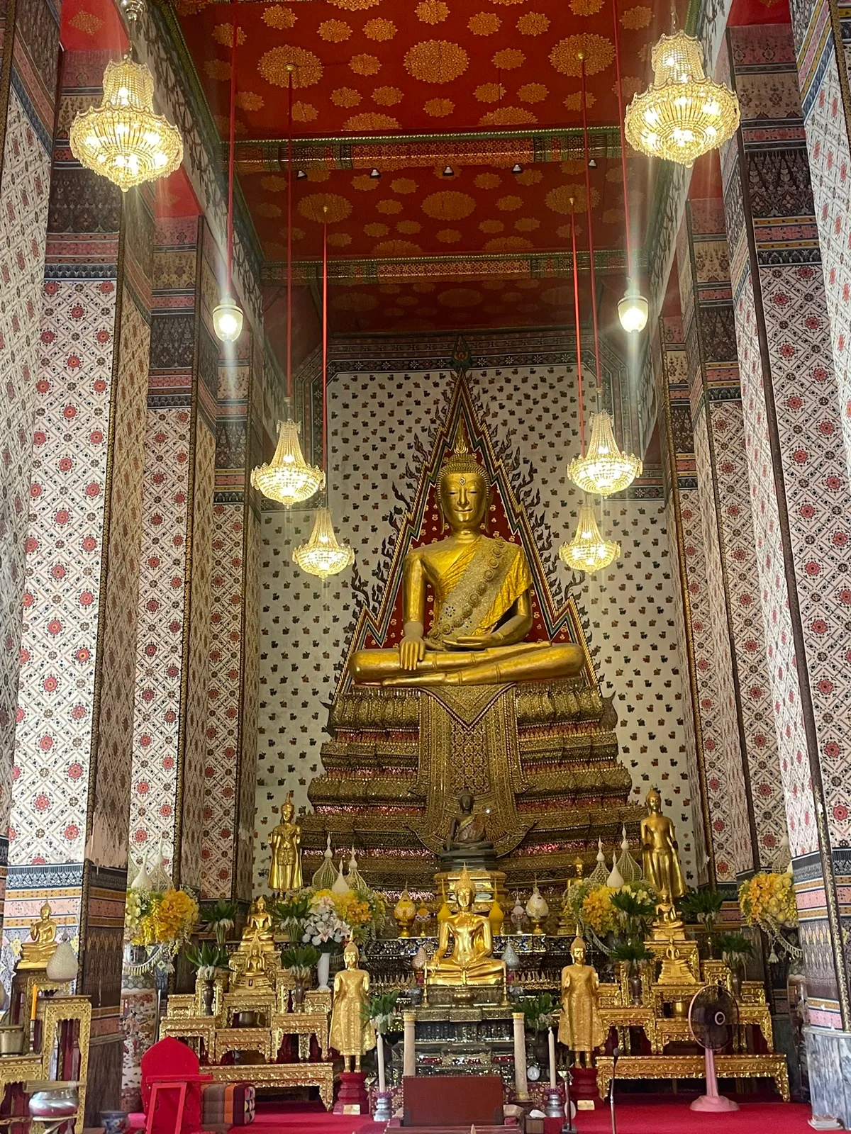 L'intérieur d'un temple : bouddha doré sous les lustres, colonnes peintes de motifs