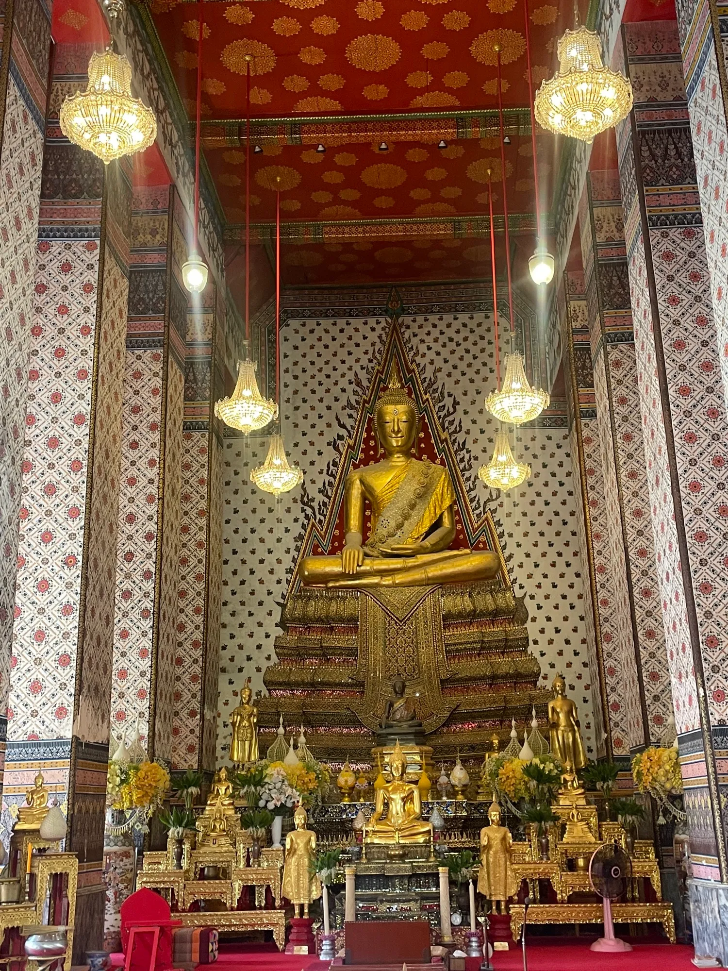 L'intérieur d'un temple : bouddha doré sous les lustres, colonnes peintes de motifs